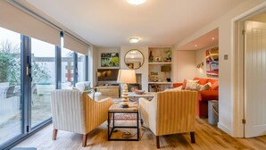 En rummelig stue med en stor skydedør til en patio, et spiseområde med bord og stole, og et hyggeligt opholdsområde med sofa og puder.