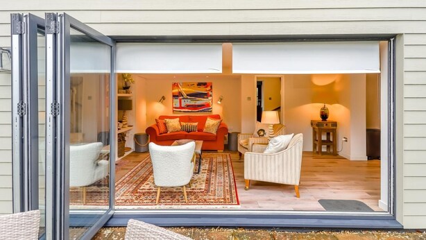 En moderne stue med en rød sofa, hvide lænestole og en farverig måtte.