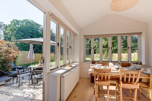 Un'ampia sala da pranzo luminosa con un tavolo apparecchiato per quattro persone, grandi finestre e vista sul giardino.
