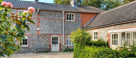 A stone house with a gravel driveway and a well-maintained hedge.