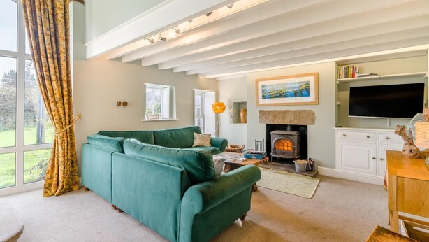 Una sala de estar con un sofá verde, una chimenea, un televisor y un ventanal con cortinas.