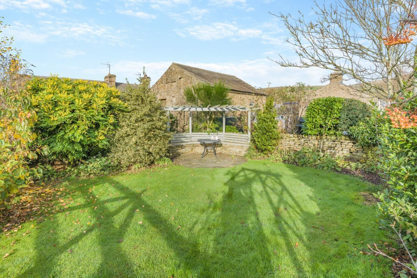 A well-maintained garden with a pergola, stone wall, and a grassy lawn.