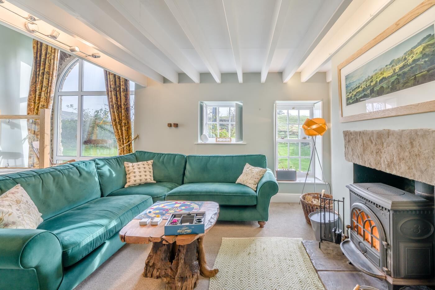 Una sala de estar acogedora con un sofá verde, una mesa de centro de madera, una chimenea y ventanas amplias con cortinas.