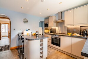 A modern kitchen with a central island, built-in oven, microwave, and stainless steel range hood. - 3 Bed in Sandsend (oc-wa081) (Sandsend)