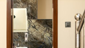 A bathroom with a marble wall, a sink, and a mirror.