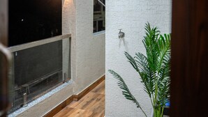 A corridor with wooden flooring, a white textured wall, and a potted plant.