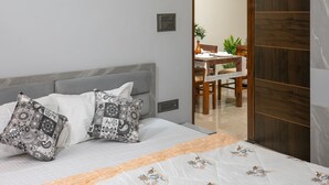 A bedroom with a bed, pillows, a bedside table, a chair, and a wooden wardrobe.