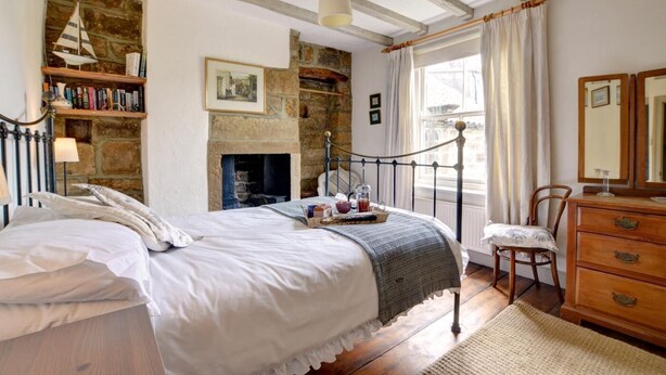 Un dormitorio con cama, cómoda, silla, estantería, chimenea y ventana con cortinas.