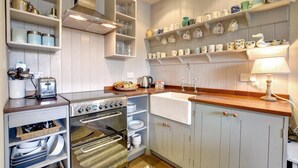 Una cocina con armarios blancos, estufa, pileta y estanterías con platos y tazas.