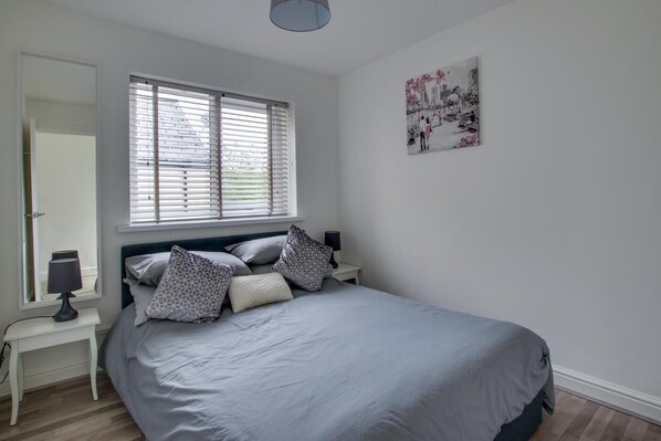 A bedroom with a bed, a bedside table with a lamp, a window with blinds, and a wall-mounted picture. - 3 Bed in Cardiff (oc-bow177) (Cardiff)