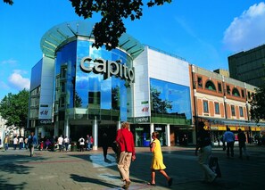 Un edificio moderno con fachada de vidrio y el letrero 'Capitol', rodeado de peatones y otros edificios comerciales.