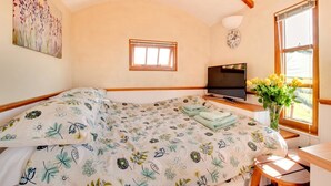 Een slaapkamer met een bed, een televisie, een klok en een raam met bloemen.