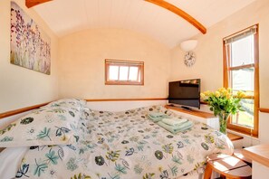 Ein Schlafzimmer mit einem Bett, einem Fernseher, einer Uhr und einem Fenster mit Blumen.
