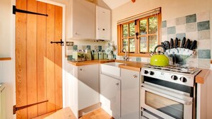 Een keuken met houten kastjes, een fornuis, een spoelbak en een raam met uitzicht op groen.
