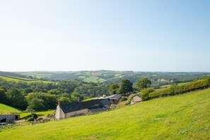 Ländliche Landschaft mit einem Haus auf einem Hügel, umgeben von Feldern und Bäumen.