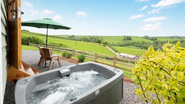 Een hottub met een houten terras, een tafel met stoelen en een groene parasol.