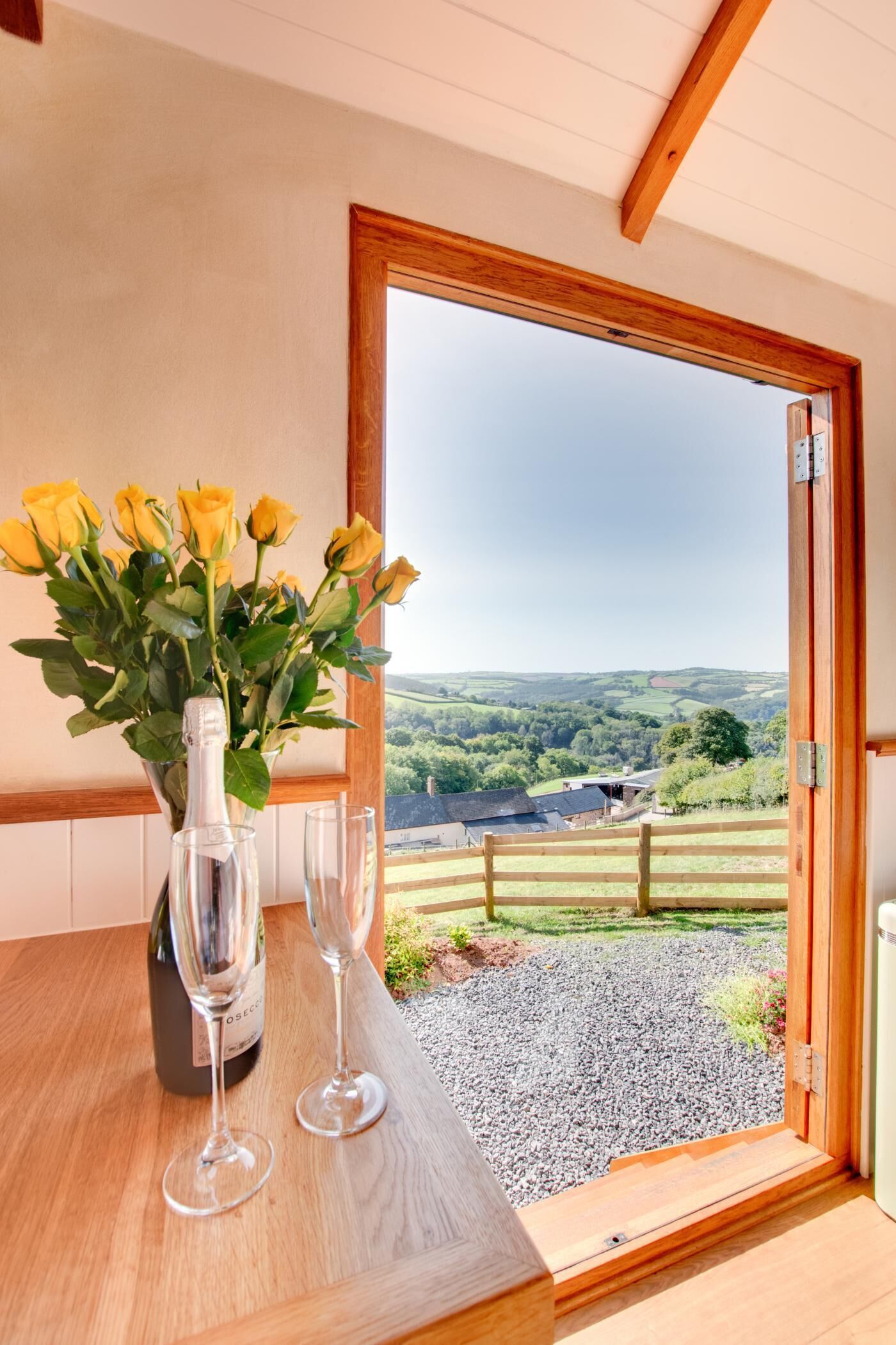 A room with a wooden table, a vase with yellow flowers, and two wine glasses.