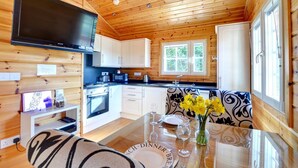 A cozy cabin interior with a wooden interior, a dining table set for two, a kitchen area with a stove and microwave, and a large window providing natural light. - 1 Bed in Pickering (oc-y290) (Middleton)