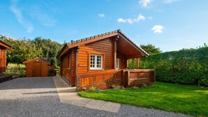 A wooden cabin with a porch, a gravel driveway, and a well-maintained lawn. - 1 Bed in Pickering (oc-y290) (Middleton)