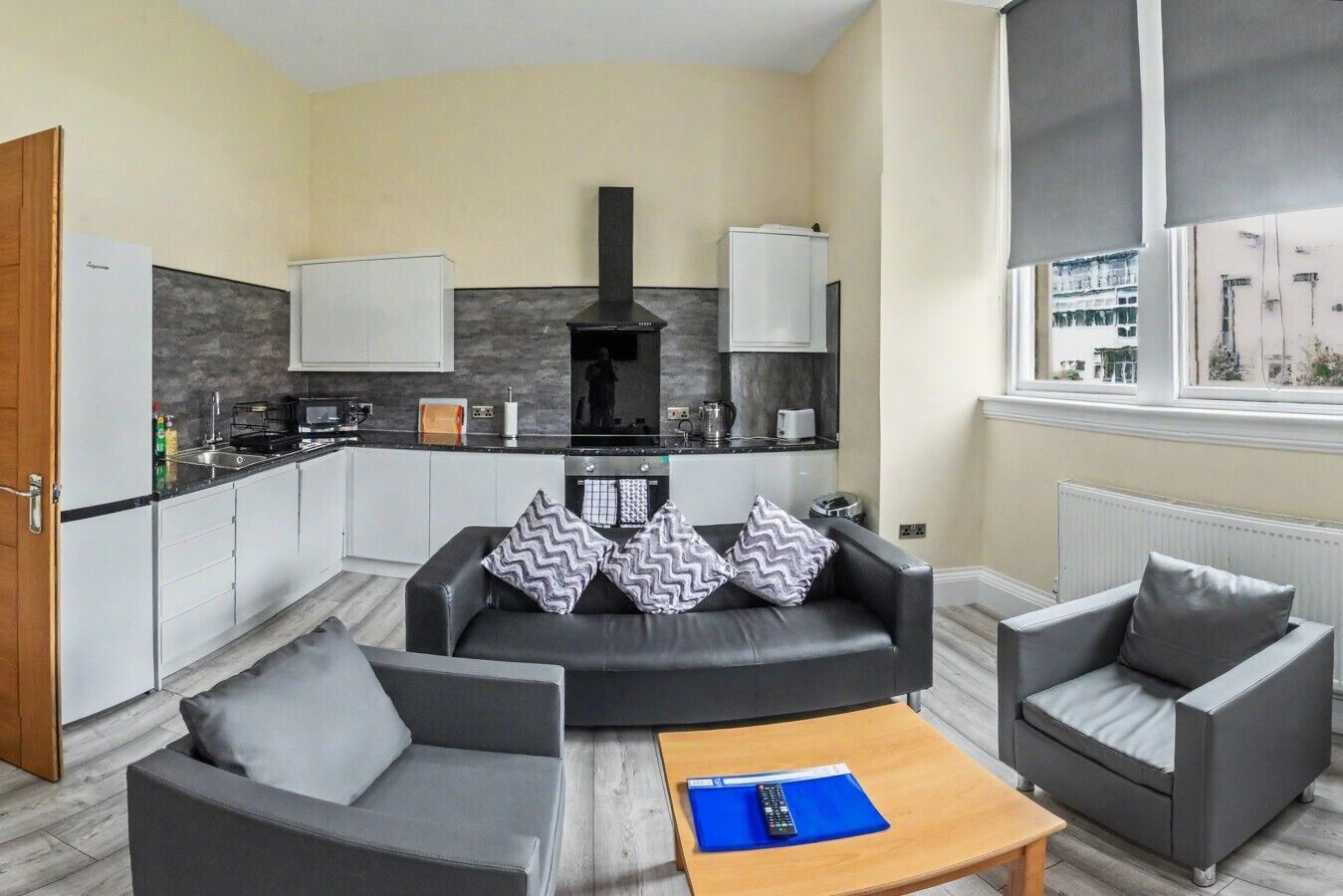 A modern living room with a sofa, two armchairs, a coffee table, and a kitchen area with a stove, oven, and cabinets.