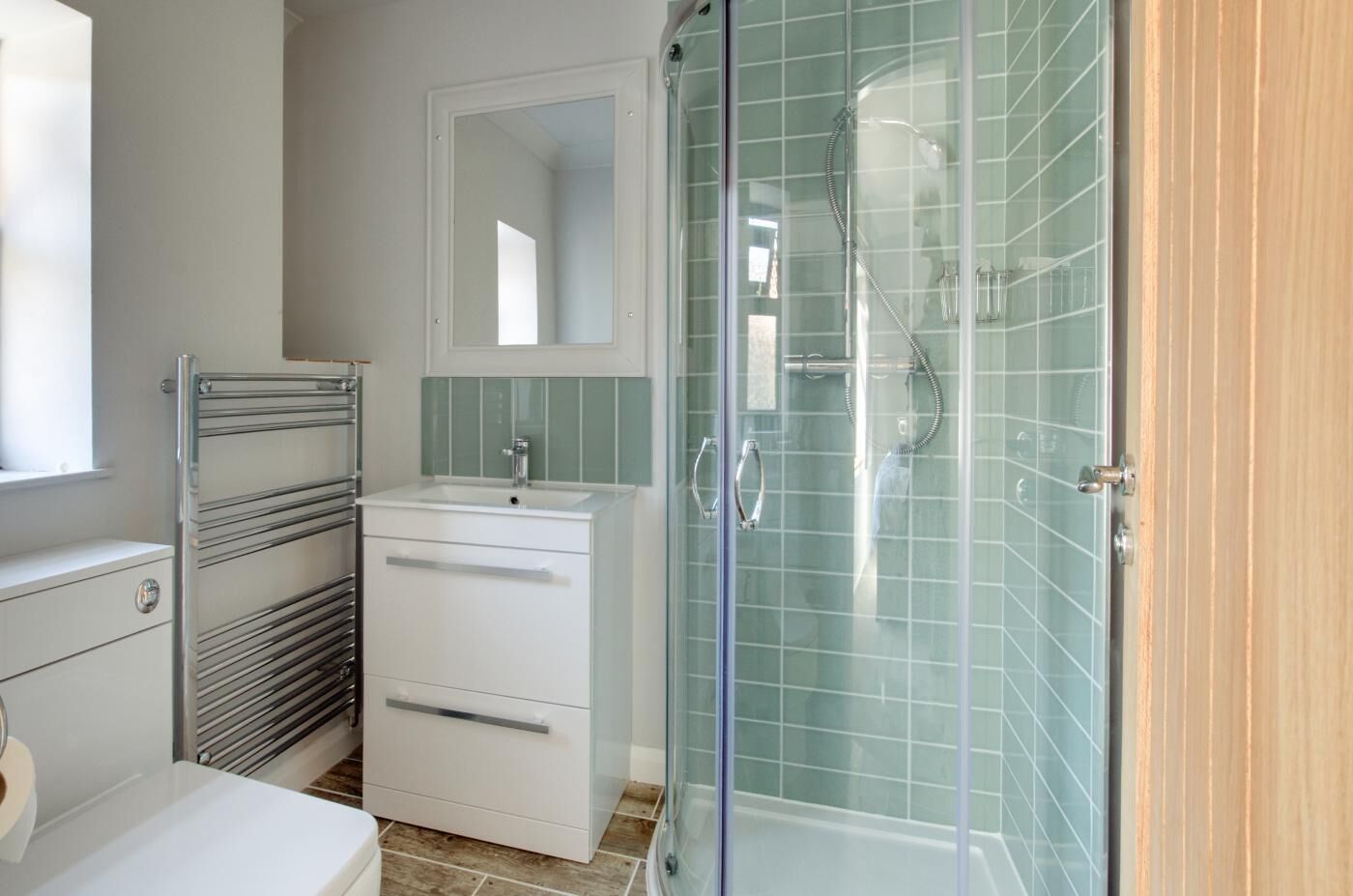 A bathroom with a glass shower enclosure, a white sink with a mirror above, and a towel rack.