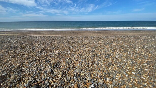 Ein Kiesstrand mit klarem Himmel und ruhiger See.