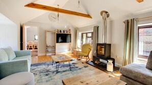 Ein geräumiges Wohnzimmer mit hoher Decke, freiliegenden Holzbalken, einem Kamin, einem Fernseher und einer gemütlichen Sitzecke.