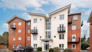 A multi-story residential building with a central entrance, balconies, and a parking area with cars. - Apartment - Sleeps 2 - Parking - City Centre Close (Coventry)