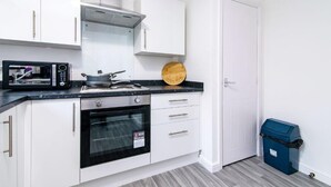 A compact kitchen with white cabinets, a microwave, an oven, and a blue trash bin. - Apartment - Sleeps 2 - Parking - City Centre Close (Coventry)