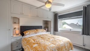 Une chambre dotée d’un grand lit, d’un ventilateur de plafond, d’étagères intégrées, d’une fenêtre avec des rideaux et offrant une vue sur l’extérieur.