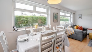 Un coin repas avec une table dressée pour quatre personnes, de grandes fenêtres, un canapé et un luminaire suspendu.