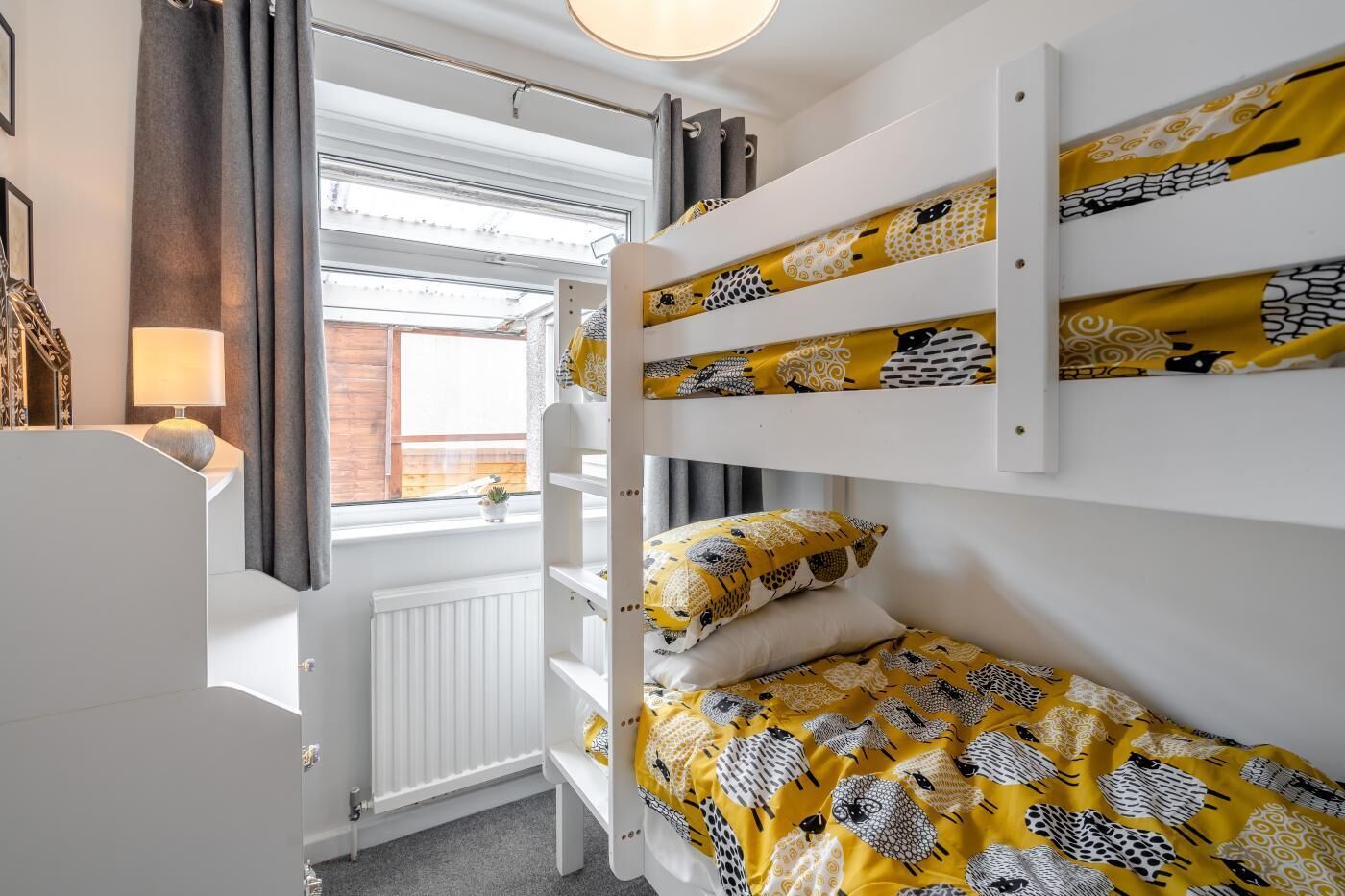 Un llit superposat amb roba de llit estampada, una làmpada de nit i una finestra amb cortines.