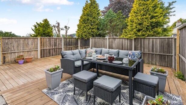 Une terrasse dotée d’une table et de chaises en osier, entourée de plantes en pot et bordée d’une plateforme en bois.