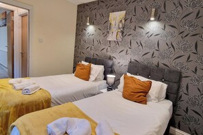 A hotel room with two beds, each with a yellow bedspread and white pillows. There is a floral wallpaper on the wall and a painting above the beds. - Coventry Retreat - Modern 2 Bed Apartment (Coventry)