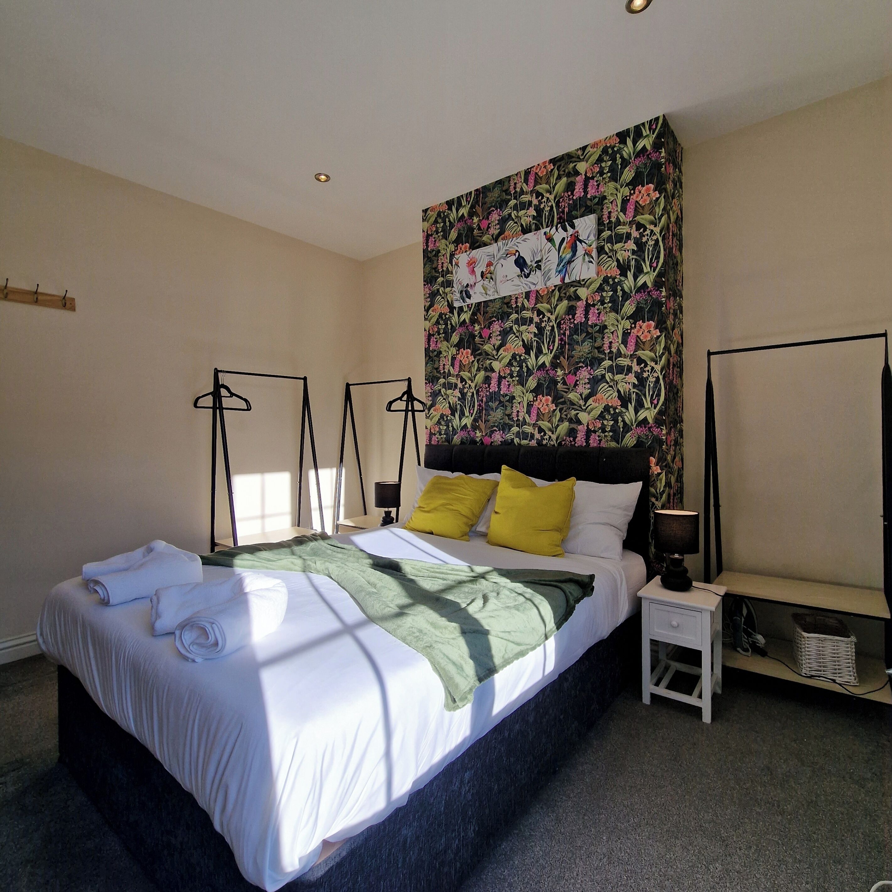 Un dormitorio con una cama grande, una mesita de noche, una lámpara de pared y un tapiz floral.
