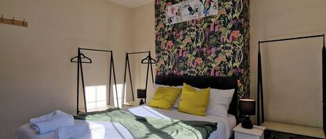 Un dormitorio con una cama grande, una mesita de noche, una lámpara de pared y un tapiz floral.