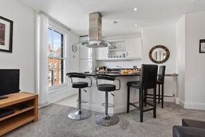 A modern kitchen with a central island, bar stools, a television, and a large window. - 2 Bed in Whitby (oc-w026) (Whitby)