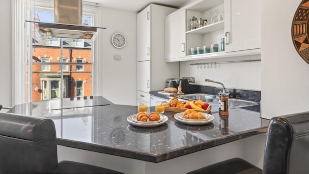 Cozinha moderna com espaço para café da manhã, incluindo croissants, frutas e suco.