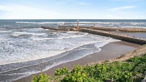 Uma paisagem costeira com um cais que se estende para o mar, um farol e uma praia de areia.