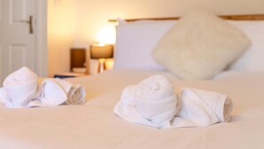 Habitación de hotel con toallas ordenadas sobre la cama, una lámpara y una puerta al fondo.