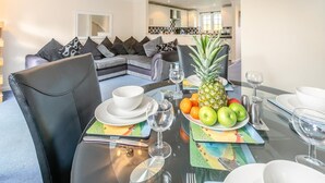 Un comedor con una mesa preparada para dos personas, que incluye una piña, manzanas y naranjas.