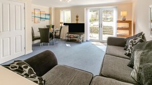Una sala de estar con sofá, televisor, mesa de comedor con sillas y puerta corrediza de vidrio que da a un espacio exterior.