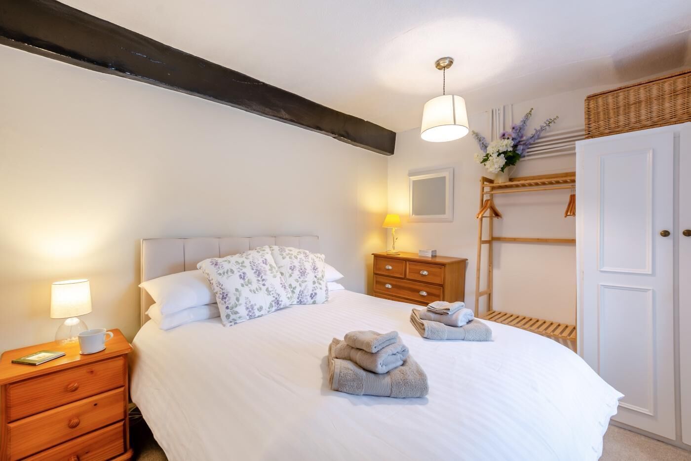 A neatly made bed with floral pillows, a bedside lamp, a wooden nightstand, and a wardrobe with a hanging rack.