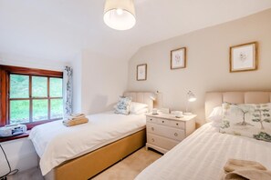 A bedroom with two beds, a bedside table with lamps, a window with curtains, and framed pictures on the wall. - 4 Bed in Satterthwaite (oc-c32334) (Satterthwaite)
