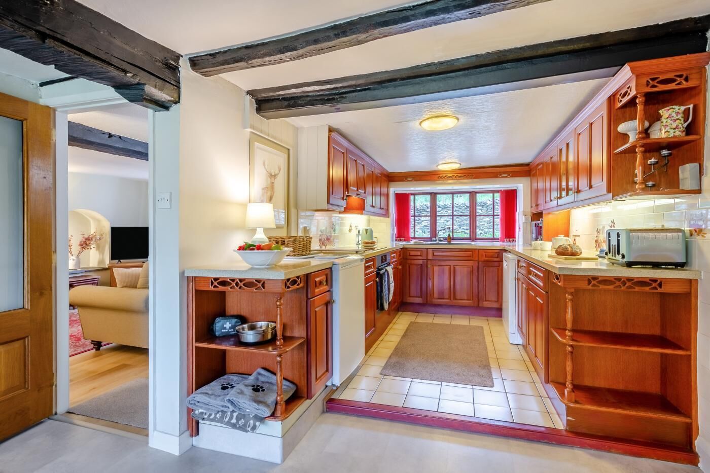 Cocina compacta con armarios de madera, una isla central y una ventana con cortinas rojas.