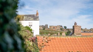Um edifício branco com telhado de telhas vermelhas, rodeado por vegetação e uma estrutura de pedra antiga ao fundo.