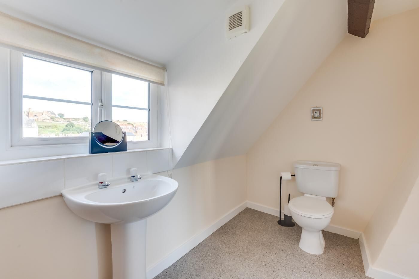 A small, clean bathroom with a white sink, a toilet, and a window with a view of buildings outside.