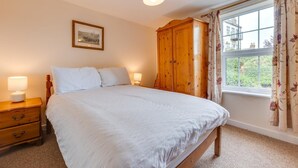 Um quarto com cama, guarda-roupa de madeira, abajures, um quadro na parede e uma janela com cortinas.