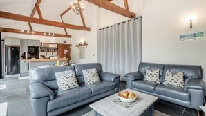 Ein modernes Wohnzimmer mit zwei grauen Ledersofas, einem Couchtisch mit Obstschale und einer Küche im Hintergrund.
