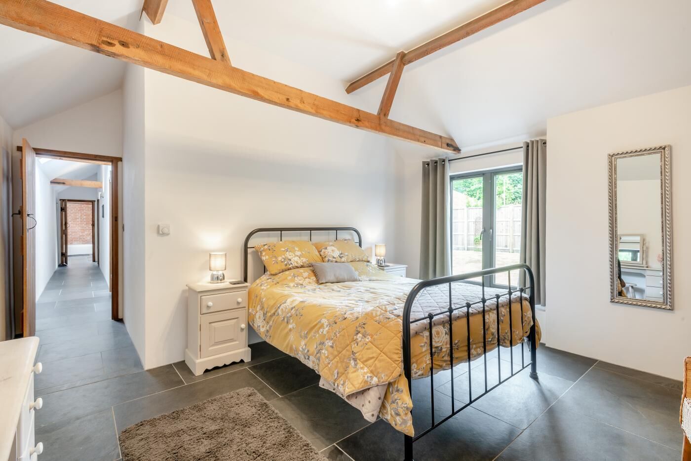 A bedroom with a bed, bedside tables, a mirror, and a view of the outside.